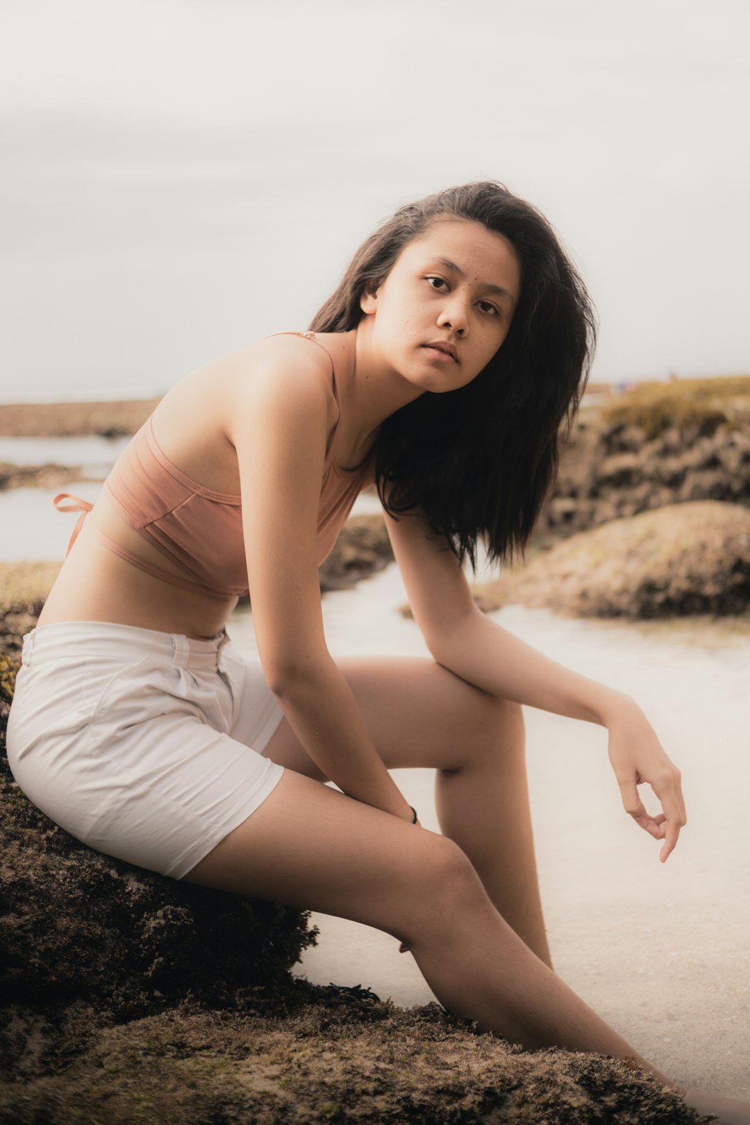 woman in white tank top and white shorts sitting on beach during daytime