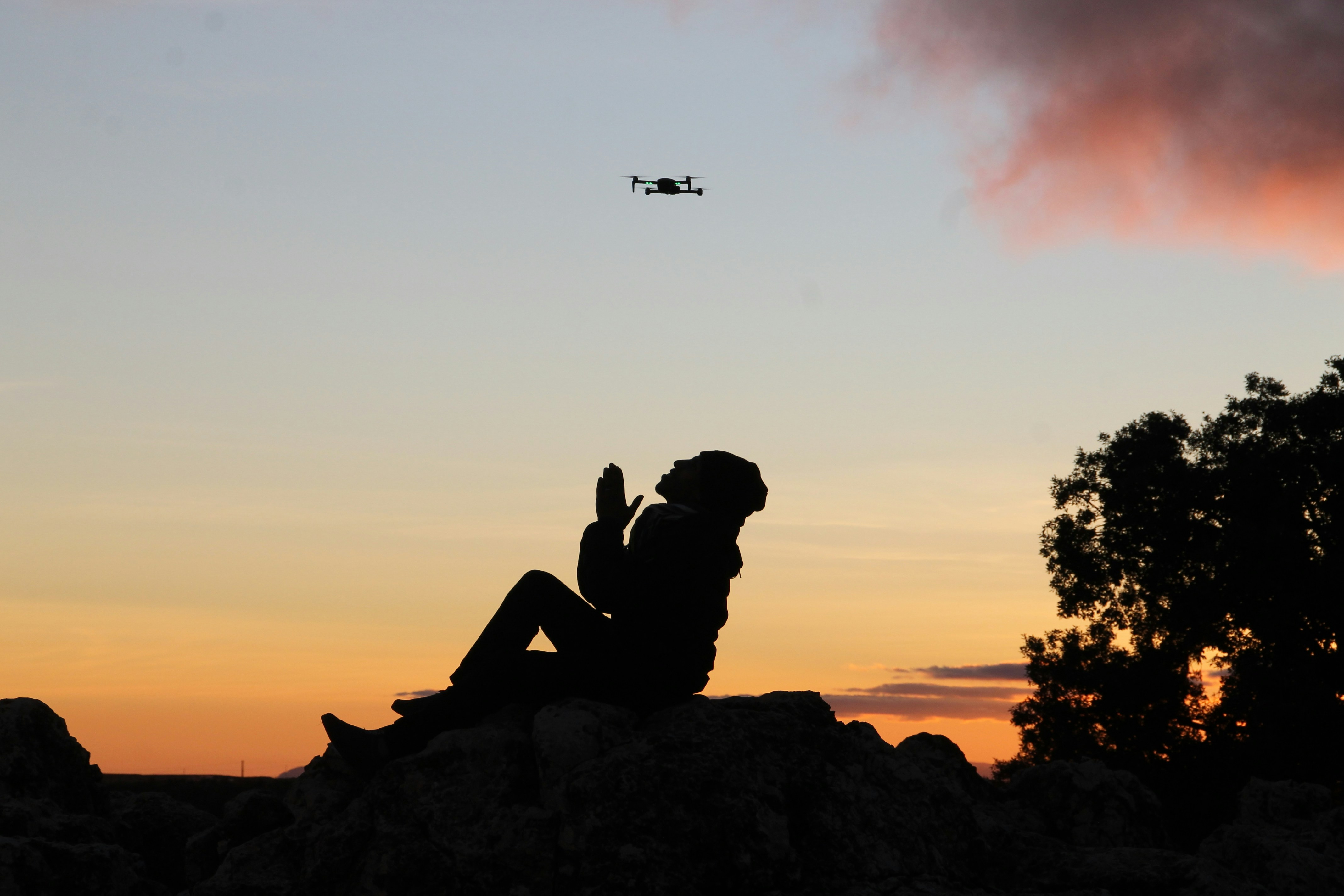silhouette of man sitting on rock during sunset