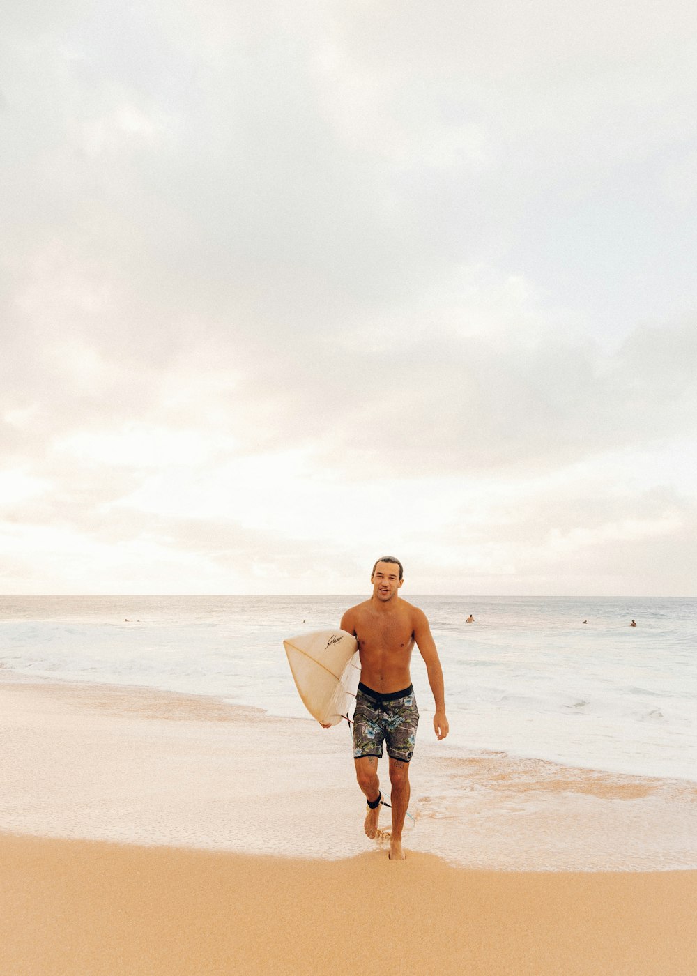 man in black shorts holding white surfboard standing on beach during daytime
