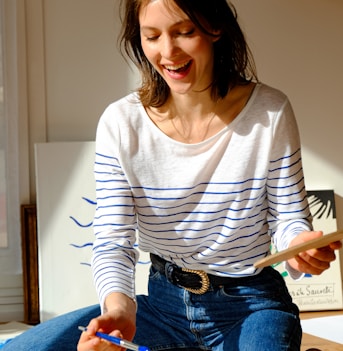 woman in white and black striped long sleeve shirt and blue denim jeans sitting on bed