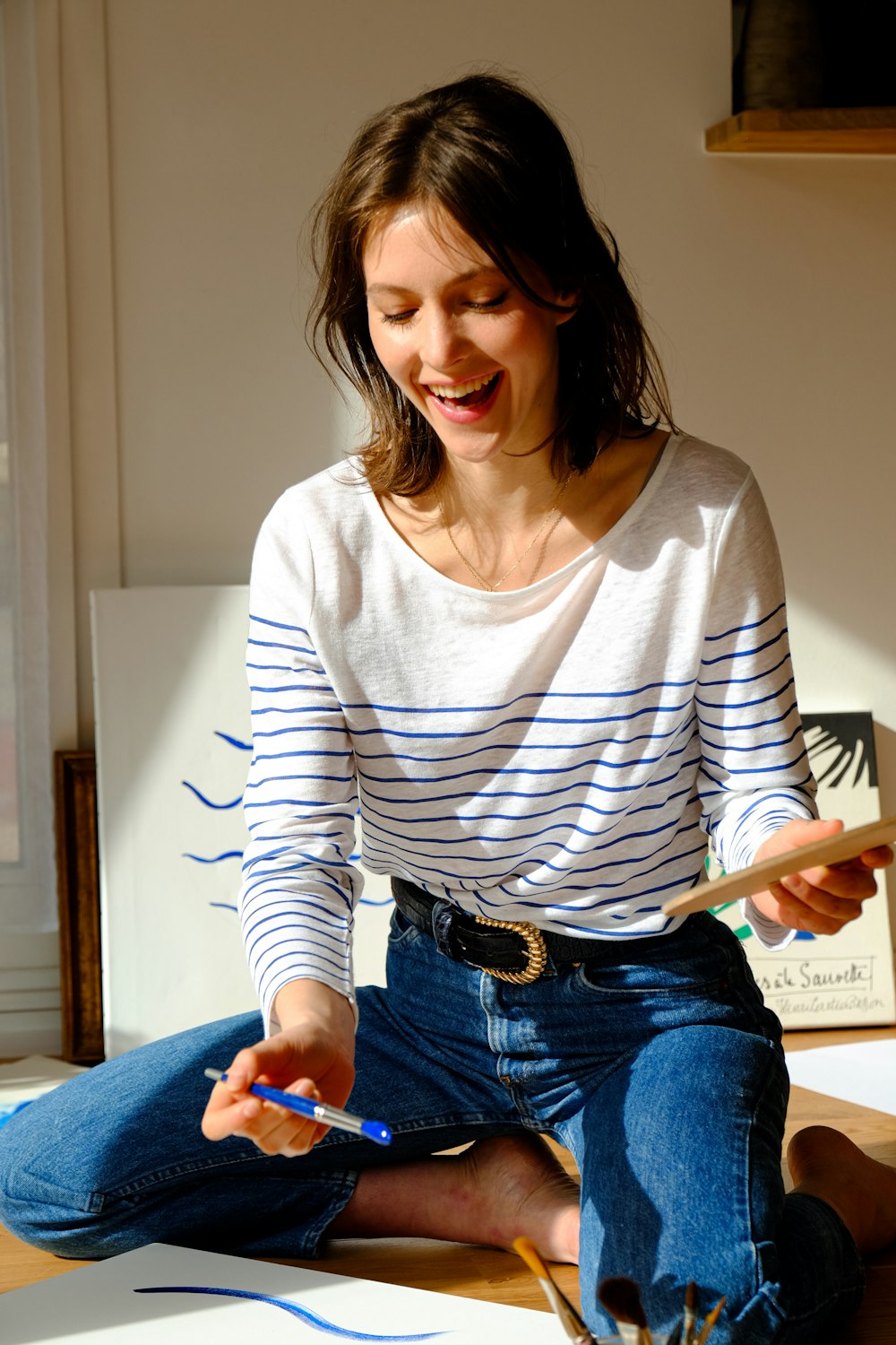 Femme en chemise à manches longues rayée blanche et noire et jean en jean bleu assise sur le lit