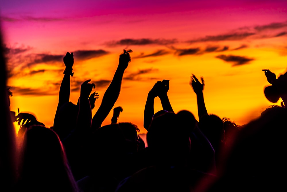 silhouette de personnes levant les mains au coucher du soleil