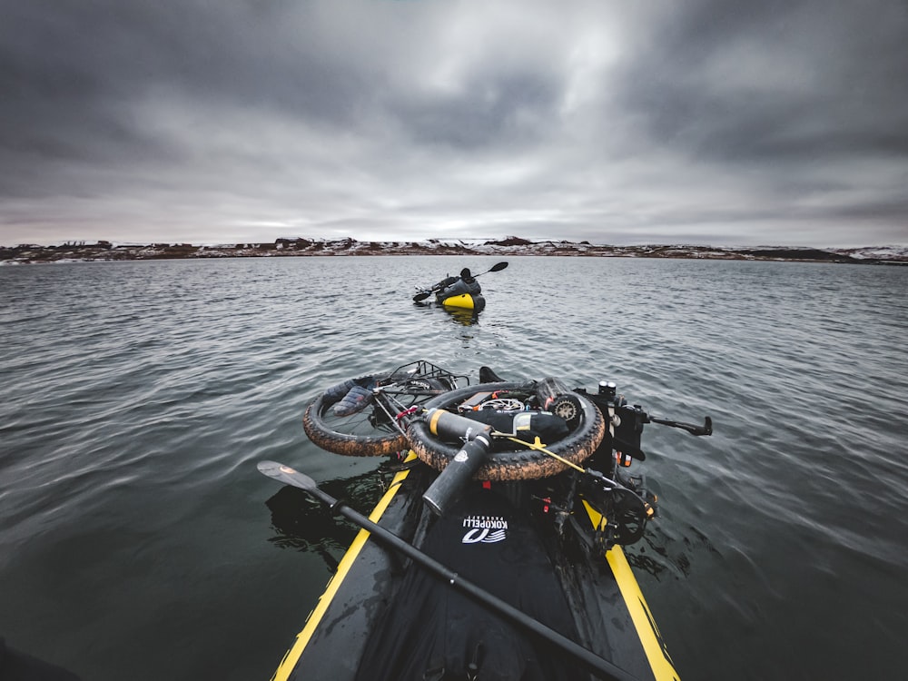 2 men riding on black and yellow boat on sea under gray clouds during daytime