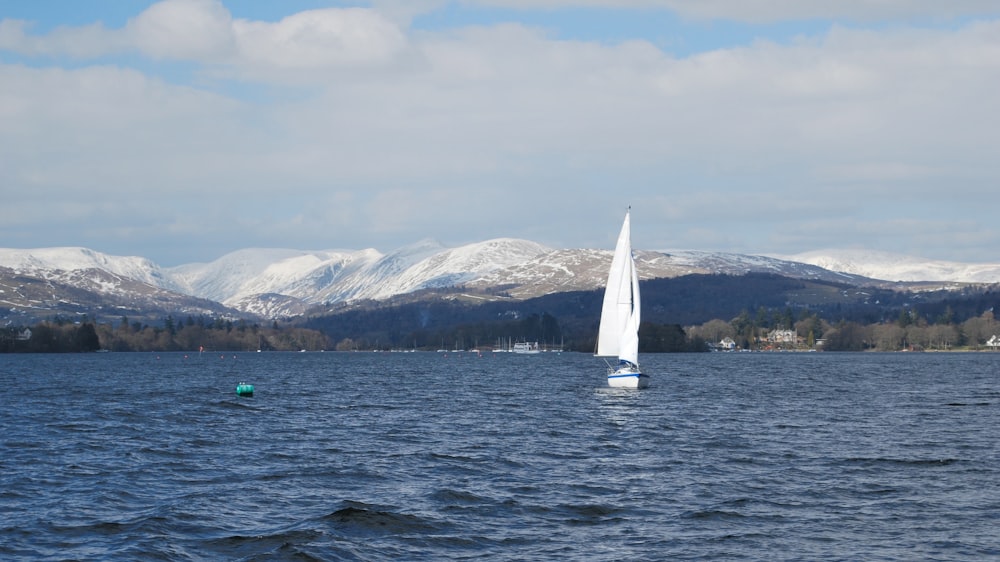white sail boat on sea near snow covered mountains during daytime