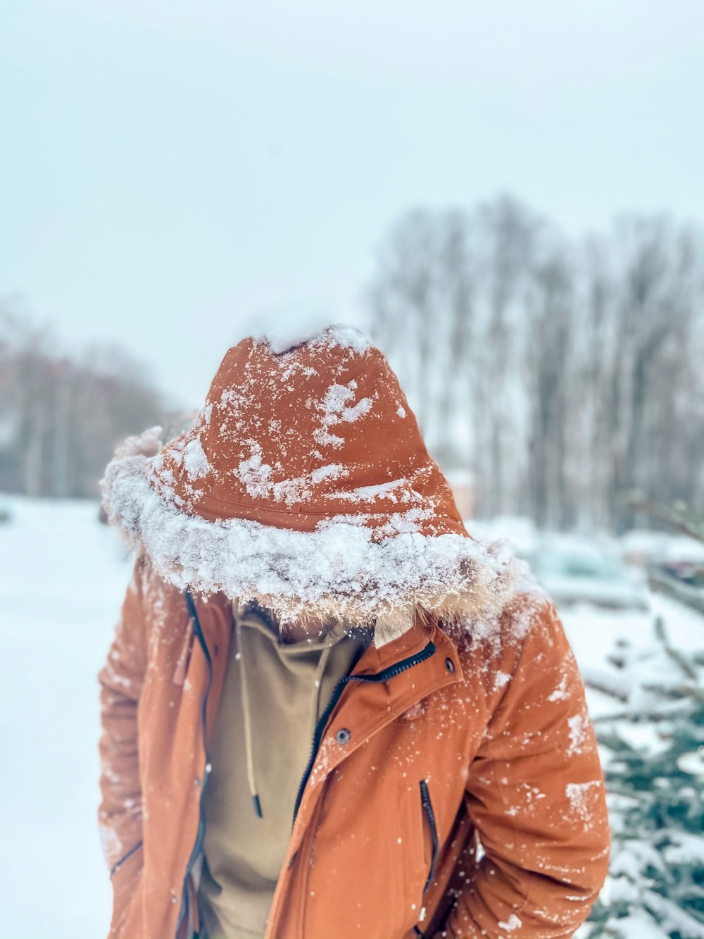 Person in braunem Kapuzenpulli, die tagsüber auf schneebedecktem Boden steht