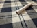 A cigarette lies on a fabric surface with a checkered pattern, featuring blue and white colors. The textile texture is clearly visible, and the cigarette appears unused with the tobacco showing at one end.