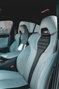 The interior of a car featuring luxury sports seats with a sleek design. The seats are predominantly light grey with black accents and have noticeable logos on the headrests. There is a spacious middle console and visible car doors showcasing a modern and upscale finish.