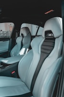 The interior of a car featuring luxury sports seats with a sleek design. The seats are predominantly light grey with black accents and have noticeable logos on the headrests. There is a spacious middle console and visible car doors showcasing a modern and upscale finish.