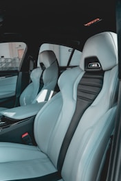 The interior of a car featuring luxury sports seats with a sleek design. The seats are predominantly light grey with black accents and have noticeable logos on the headrests. There is a spacious middle console and visible car doors showcasing a modern and upscale finish.