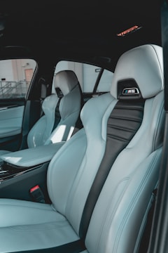 The interior of a car featuring luxury sports seats with a sleek design. The seats are predominantly light grey with black accents and have noticeable logos on the headrests. There is a spacious middle console and visible car doors showcasing a modern and upscale finish.