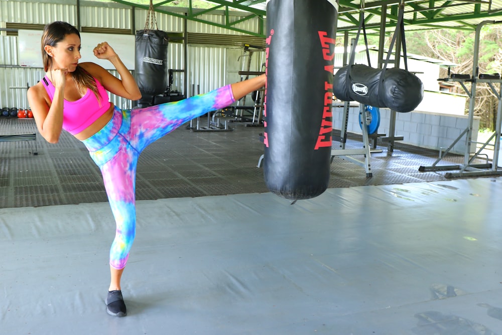 woman in pink tank top and purple shorts standing beside black heavy bag