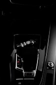 A dark car interior featuring a center console with a bottle of car refreshment placed in the cup holder. The image highlights sleek designs with glossy surfaces and visible gear shift and control knobs.