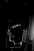 A dark car interior featuring a center console with a bottle of car refreshment placed in the cup holder. The image highlights sleek designs with glossy surfaces and visible gear shift and control knobs.