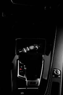 A dark car interior featuring a center console with a bottle of car refreshment placed in the cup holder. The image highlights sleek designs with glossy surfaces and visible gear shift and control knobs.