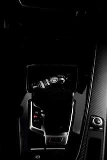 A dark car interior featuring a center console with a bottle of car refreshment placed in the cup holder. The image highlights sleek designs with glossy surfaces and visible gear shift and control knobs.
