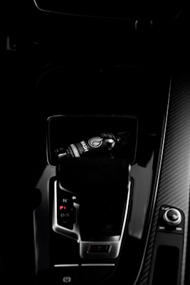 A dark car interior featuring a center console with a bottle of car refreshment placed in the cup holder. The image highlights sleek designs with glossy surfaces and visible gear shift and control knobs.
