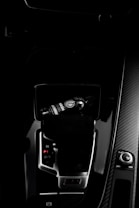 A dark car interior featuring a center console with a bottle of car refreshment placed in the cup holder. The image highlights sleek designs with glossy surfaces and visible gear shift and control knobs.