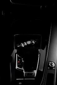 A dark car interior featuring a center console with a bottle of car refreshment placed in the cup holder. The image highlights sleek designs with glossy surfaces and visible gear shift and control knobs.