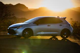 A sleek rental car parked beside a scenic mountain road at sunset.