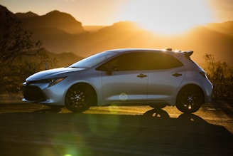 A sleek luxury car parked on a desert road at sunset.