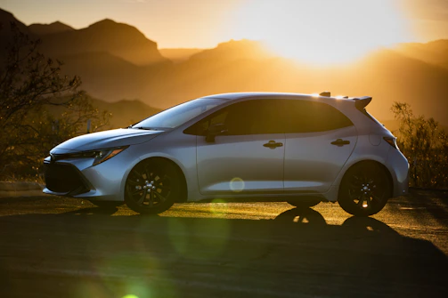 A sleek rental car parked beside a scenic mountain road at sunset.