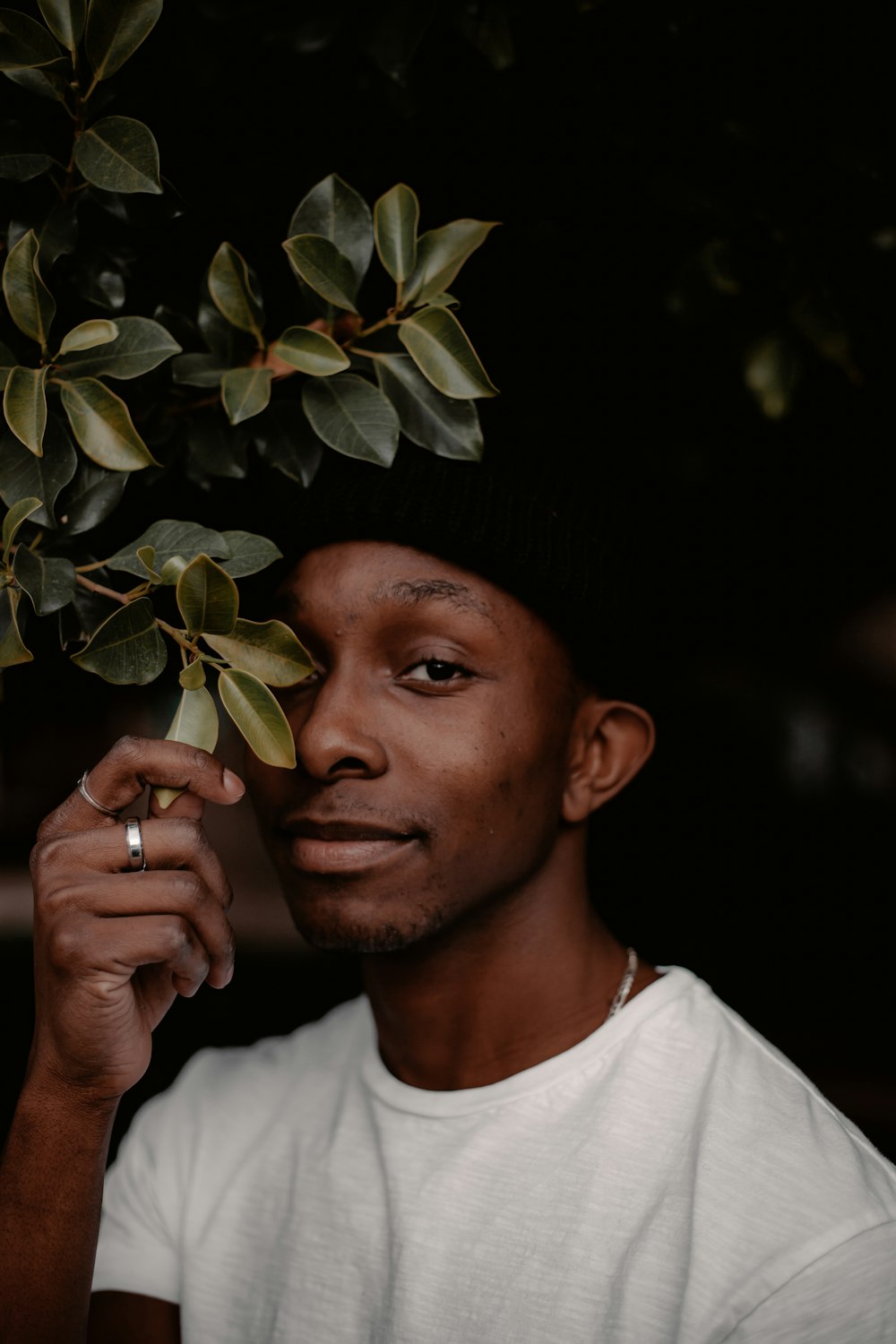 man in white crew neck shirt and black knit cap holding green leaves