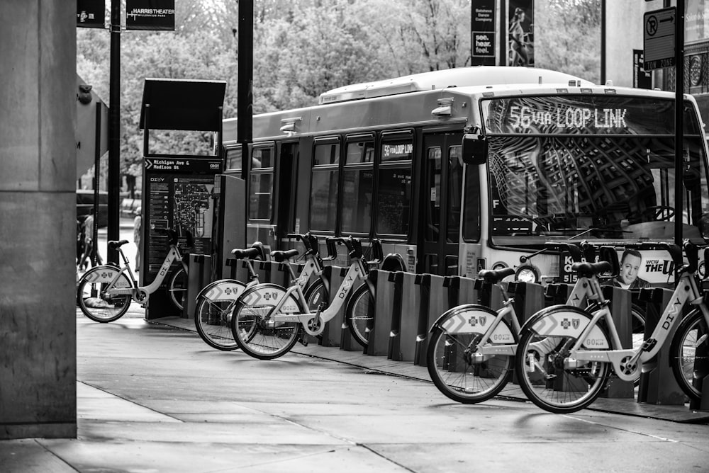 grayscale photo of city bikes parked beside building