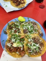 Bright blue ceramic plate holding a variety of tacos with different fillings, garnished with lime wedges and cilantro.