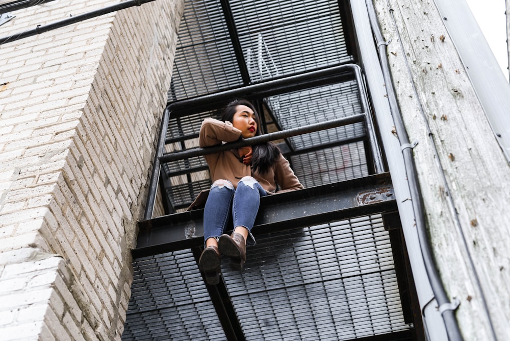 woman in blue denim jacket and blue denim jeans sitting on black metal window frame during