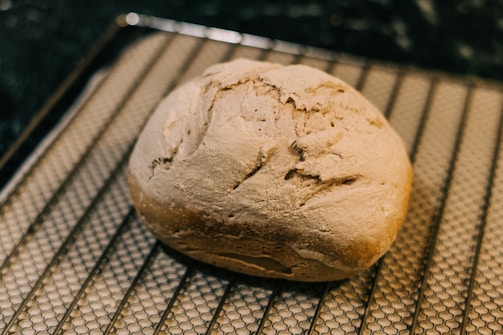 A close-up of a freshly baked golden-brown loaf of bread cooling on a wooden rack in a cozy kitchen.