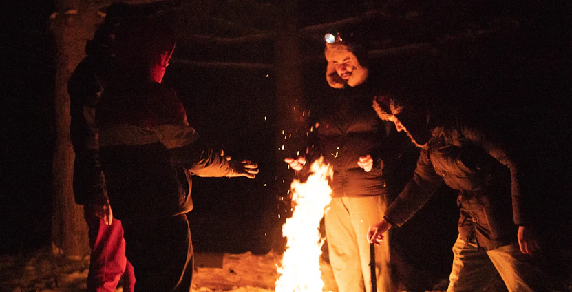 A family gathered around a campfire practicing survival skills in a forest setting.