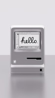 Miniaturní staromódní iMac s nápisem 'hello' na obrazovce.