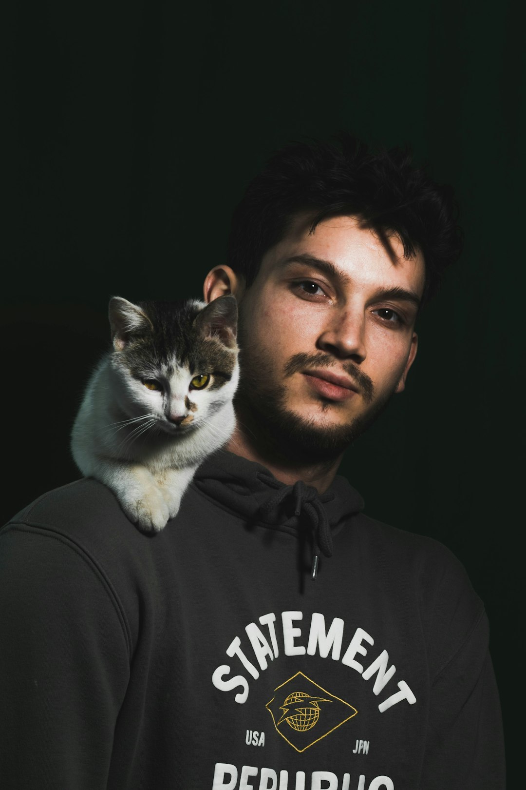 man in black hoodie holding white and black cat