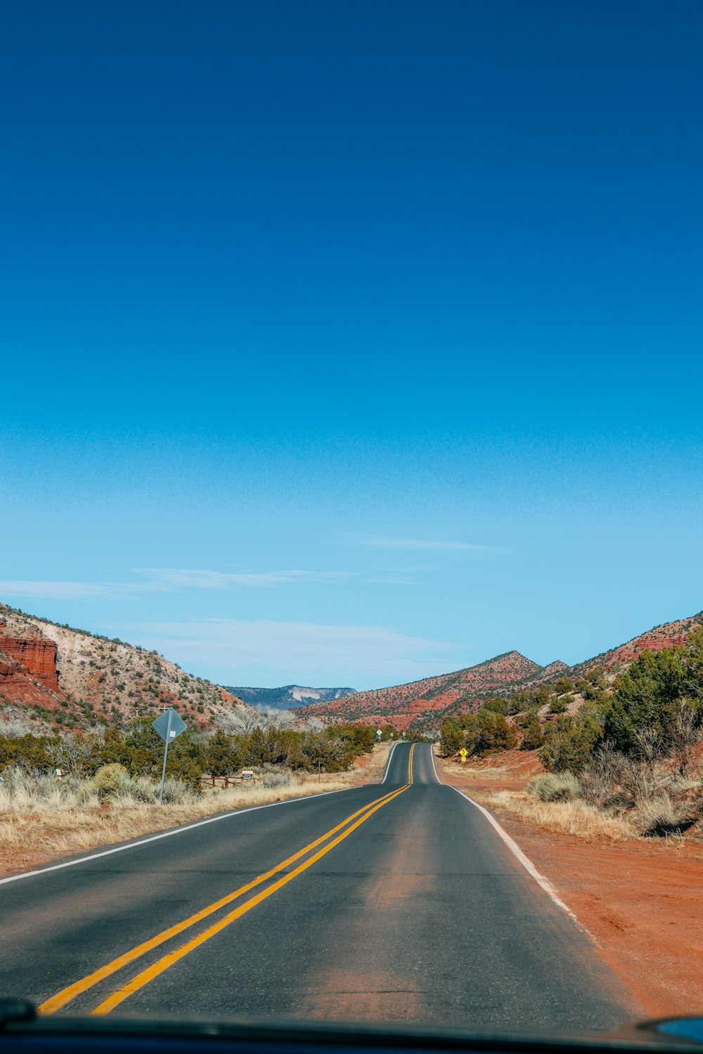 gray asphalt road between brown and green mountains under blue sky during daytime