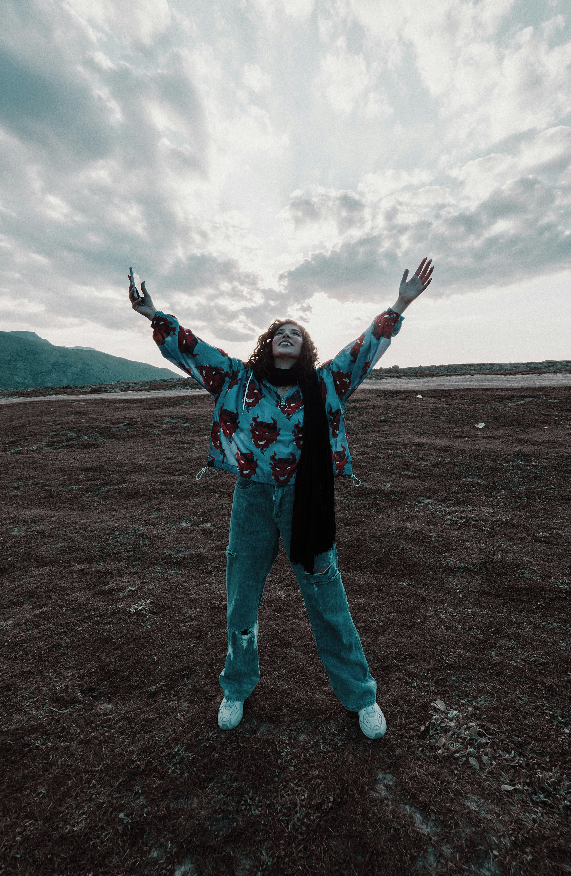 wanita dengan jaket biru dan merah dan jeans denim biru berdiri di lapangan coklat di siang hari