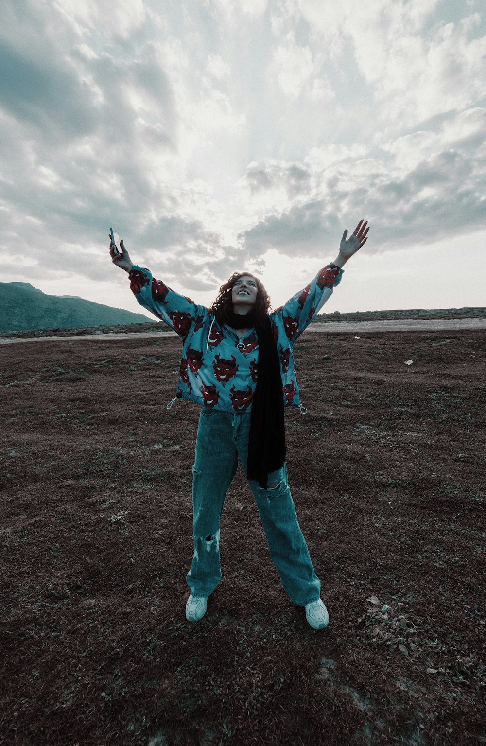 woman in blue and red jacket and blue denim jeans standing on brown field during daytime