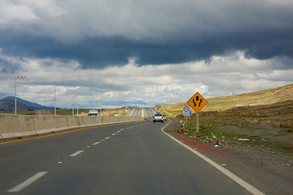 yellow and black road sign near road under white clouds and blue sky during daytime
