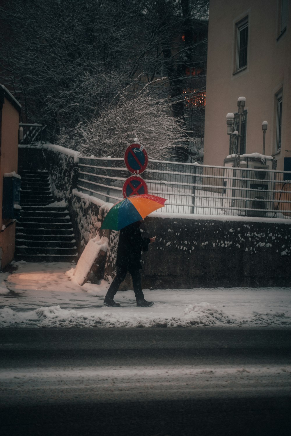 Persona in giacca nera che tiene l'ombrello rosso che cammina sulla strada innevata durante il giorno