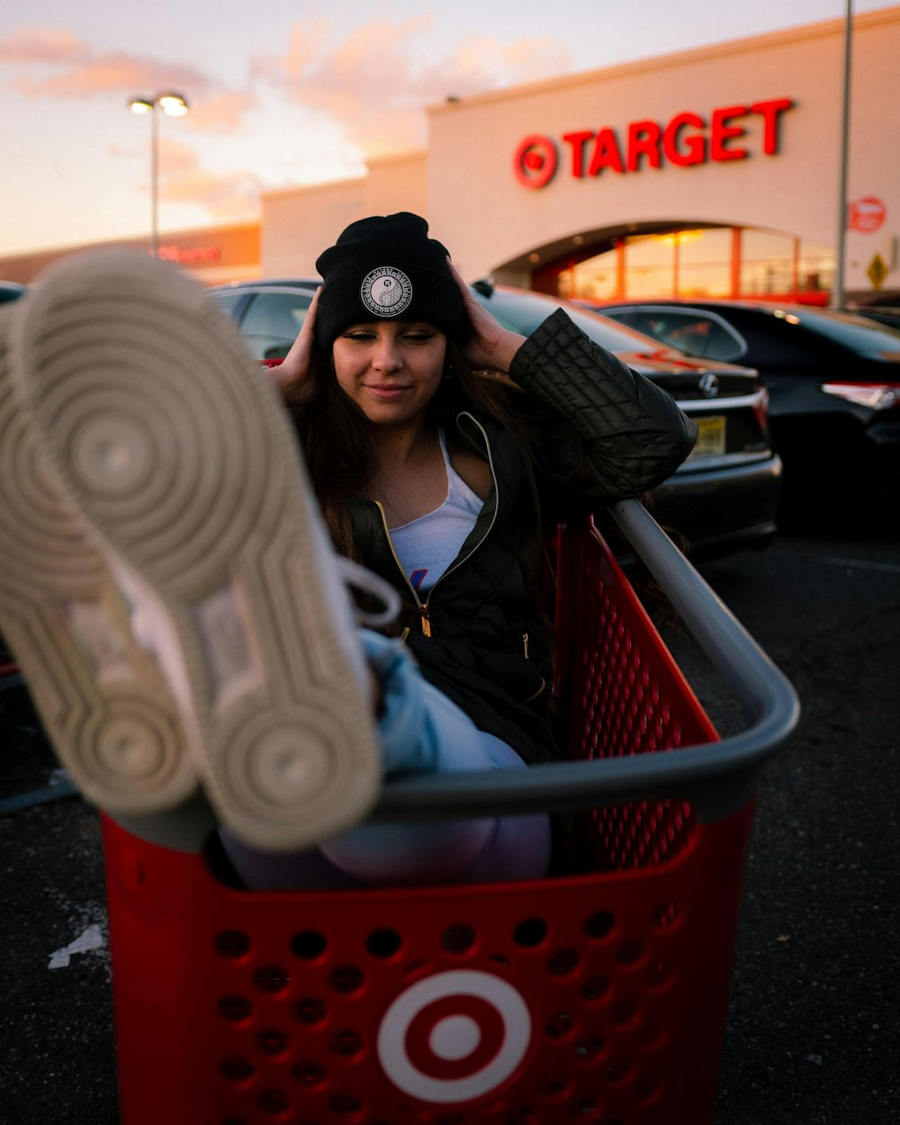 woman in black jacket sitting on red plastic shopping cart