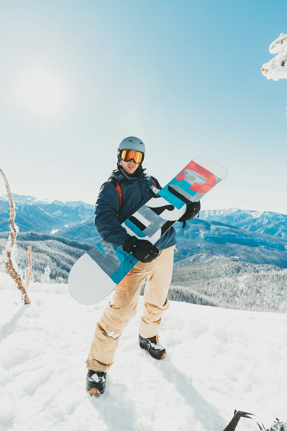 man in black jacket and brown pants carrying black and white backpack standing on snow covered