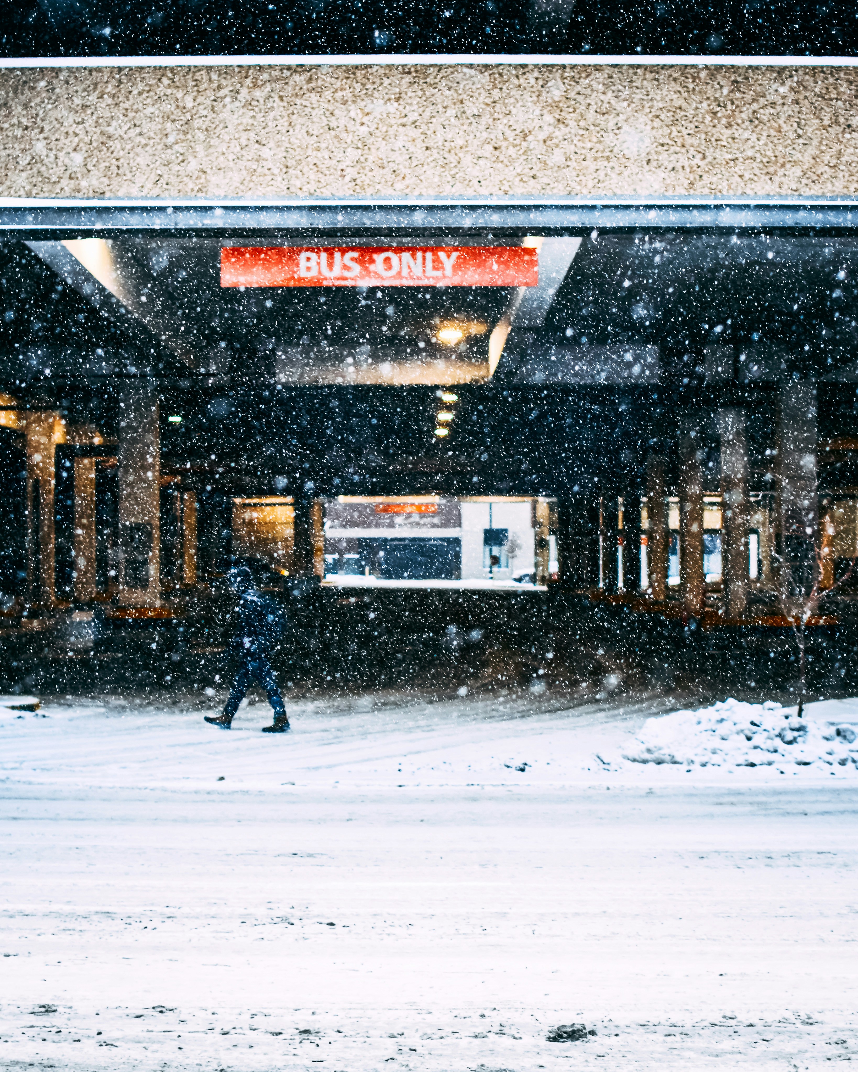 person walking on snow covered road near brown building during daytime