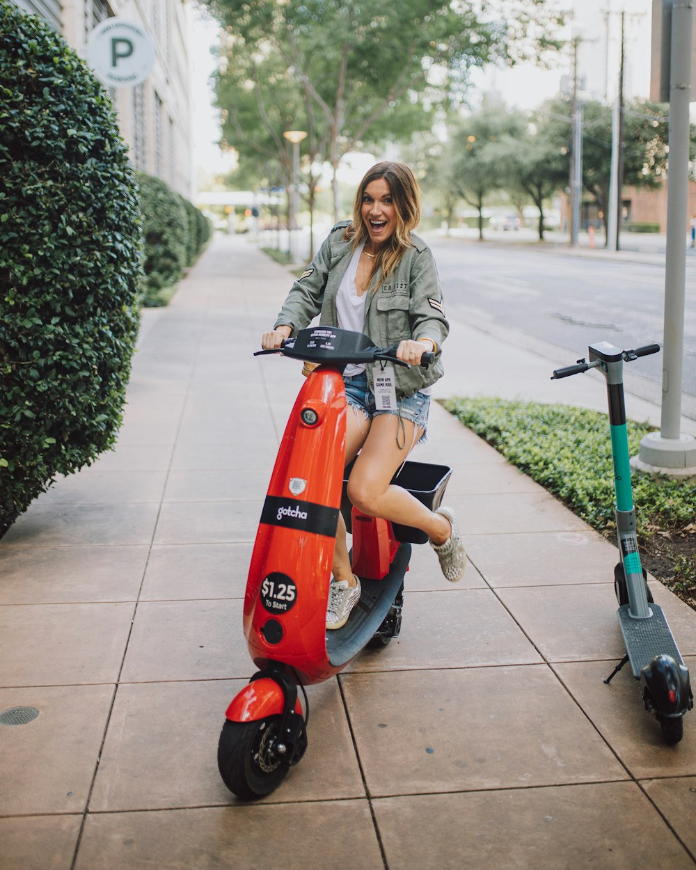 woman in gray jacket riding red and black motor scooter