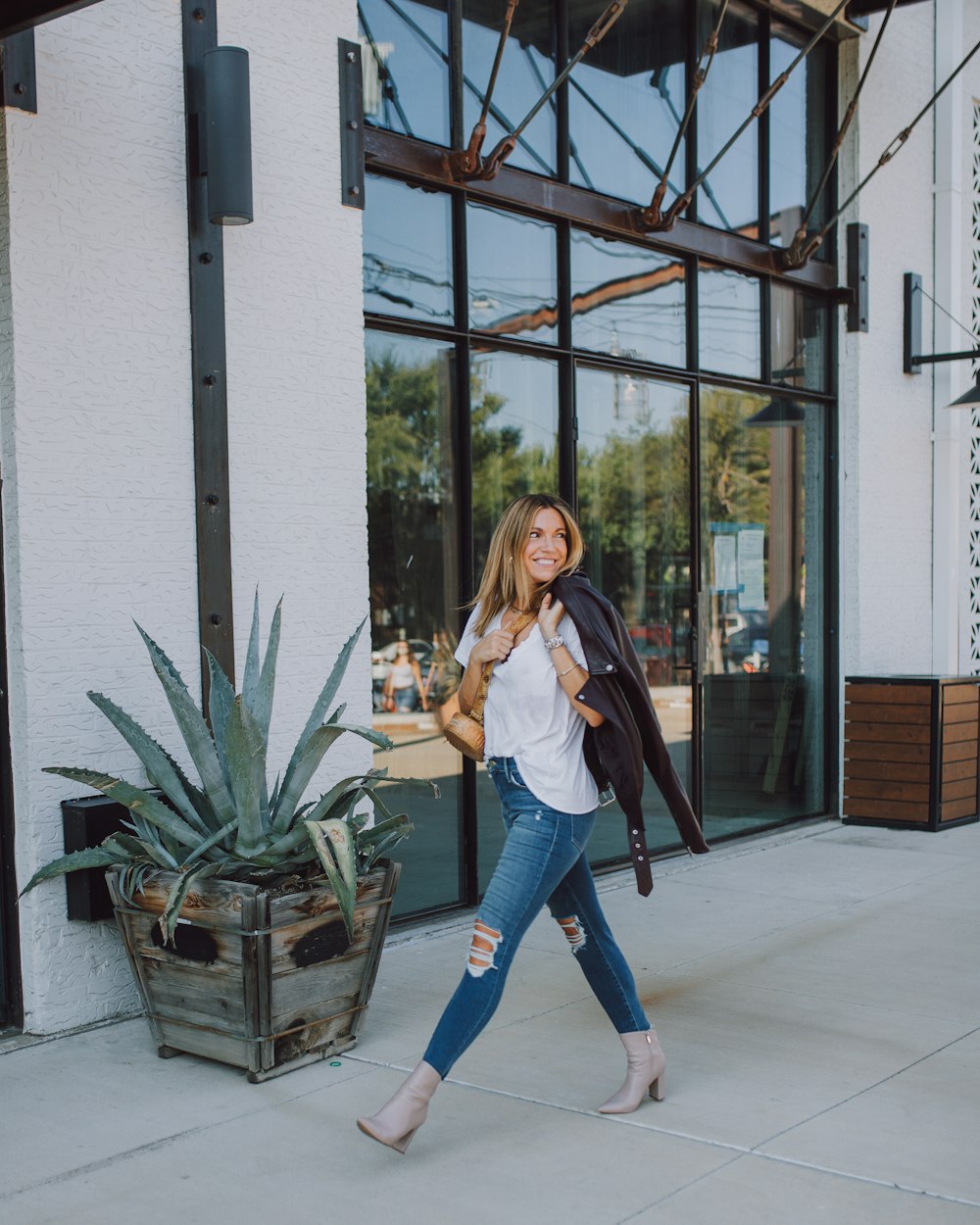 woman in black jacket and blue denim jeans standing beside green plant