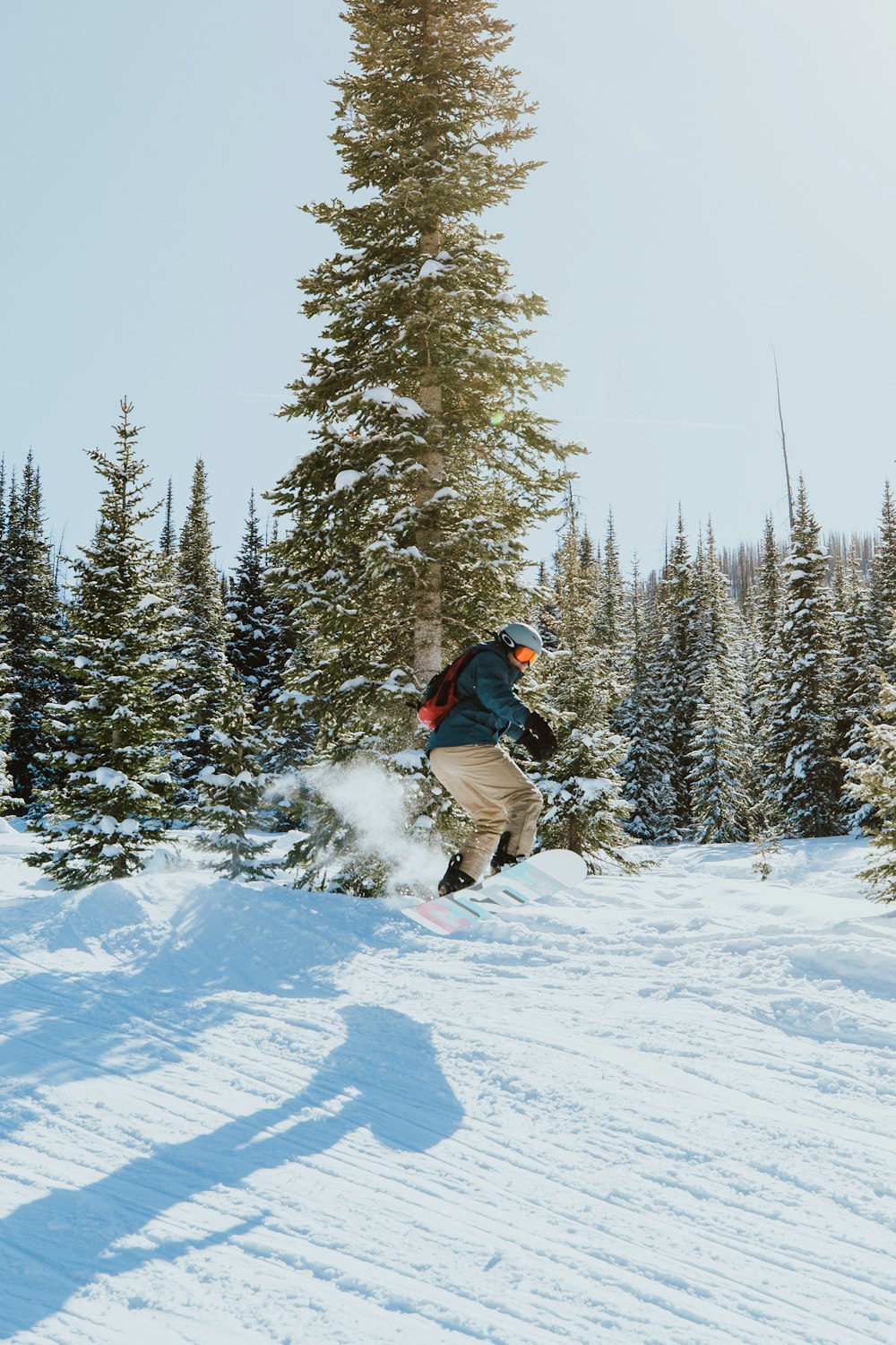 Hombre con chaqueta negra y pantalones marrones montando en snowboard en suelo cubierto de nieve durante el día