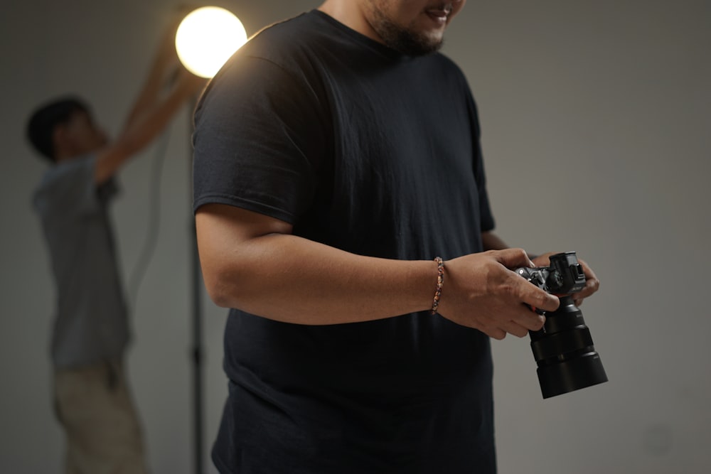 Hombre con camiseta negra de cuello redondo sosteniendo una cámara DSLR negra