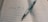 An open lined notebook with Japanese writing is placed on a surface. A pen, designed with a silver barrel and a black grip, lies diagonally across the pages.