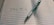 An open lined notebook with Japanese writing is placed on a surface. A pen, designed with a silver barrel and a black grip, lies diagonally across the pages.