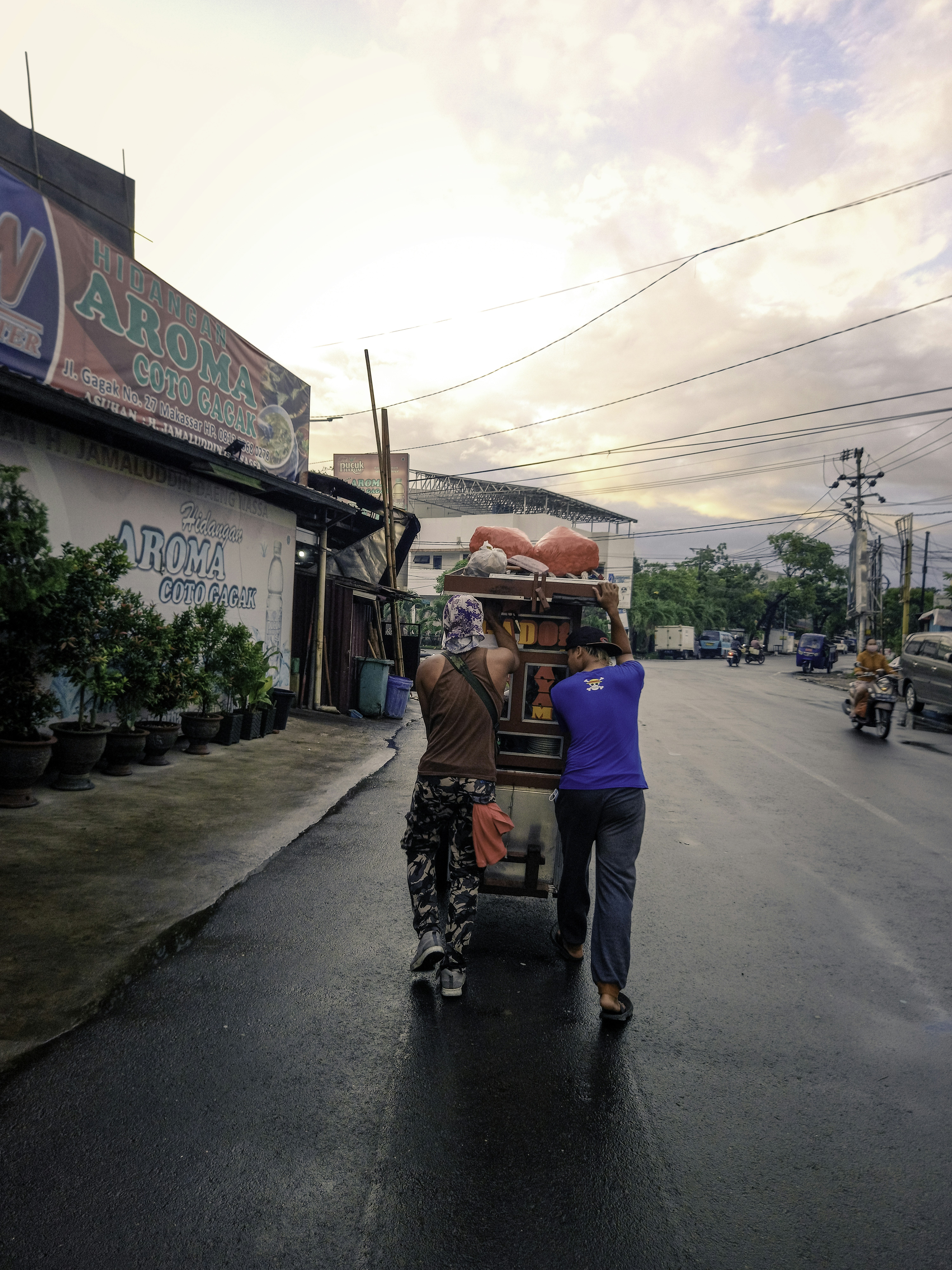 Pria dengan kemeja biru dan jeans denim biru mengendarai gerobak biru dan merah di siang hari