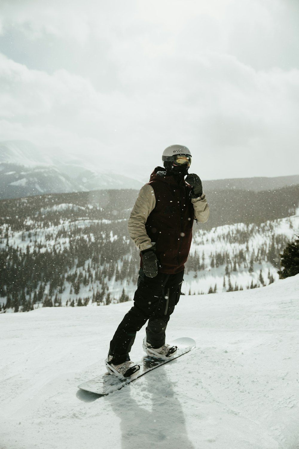 man in brown jacket and black pants standing on snow covered ground during daytime