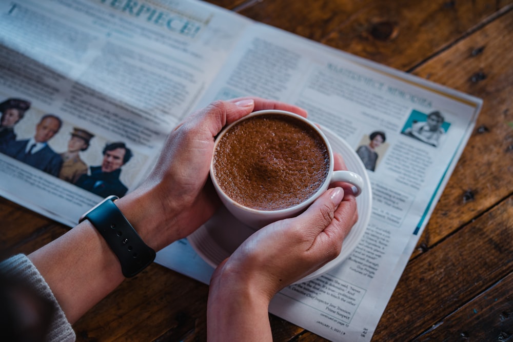 person holding white ceramic mug with brown liquid